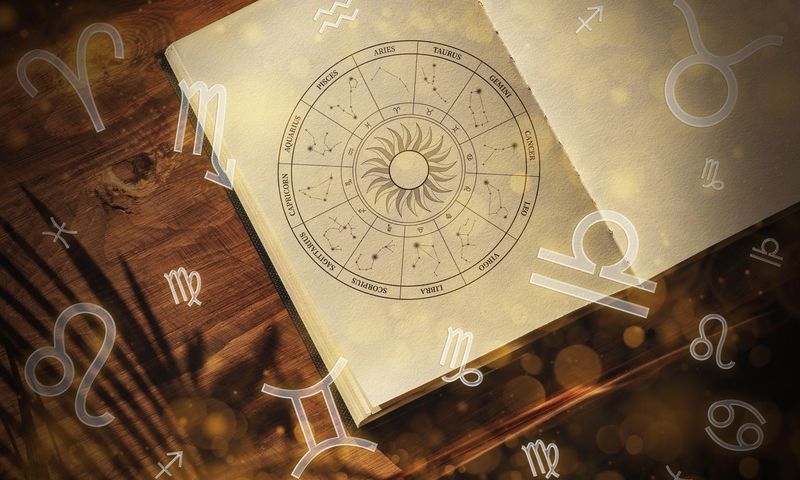 Chart of zodiac signs and astrology symbols on a wooden surface with sunlight reflecting around